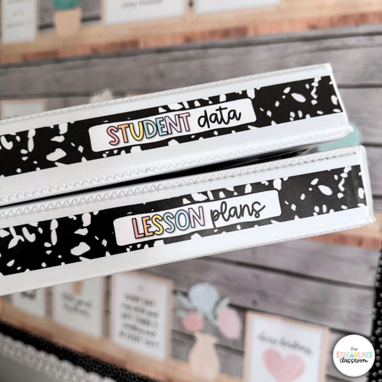 Close-up of two white binders with printed spines labeled 'Student Data' and 'Lesson Plans' in pastel rainbow text against a black composition notebook-style background, with a blurred bulletin board in the background.
