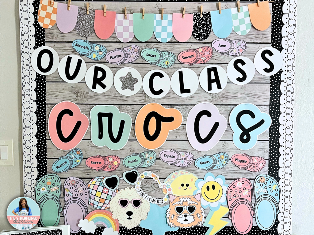 A colorful classroom bulletin board with a theme inspired by Crocs shoes. The board reads 'Our Class Crocs' in bold, playful letters on a rustic wood background, with students’ names written on small Crocs-themed name tags. Decorative elements include cute animal faces, smiley faces, rainbows, and fun, patterned paper cutouts hung on a string with clothespins. The border features a black and white doodle-style design.