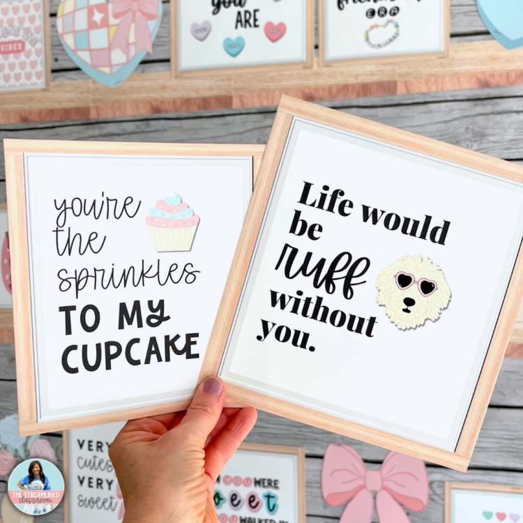 A teacher holding two framed Valentine’s quote prints—one reading "You’re the sprinkles to my cupcake" with a pastel cupcake, and the other saying "Life would be ruff without you" with a dog wearing heart-shaped sunglasses.