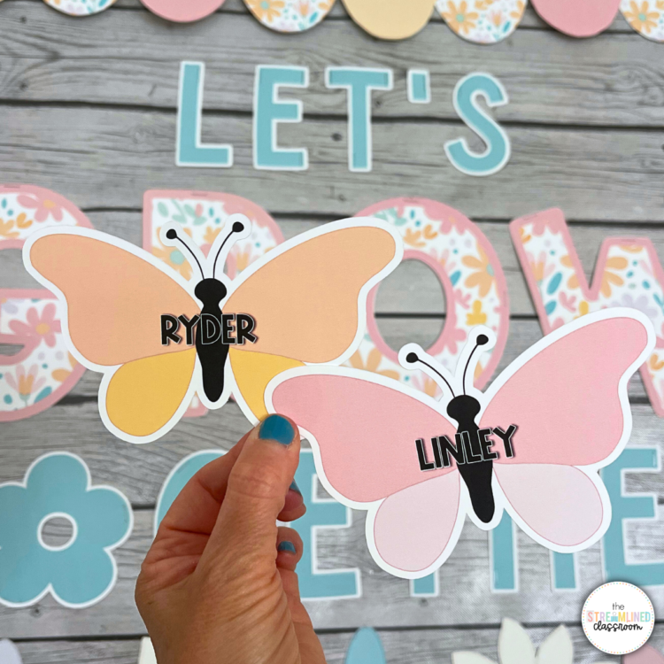 Editable butterfly name pieces for the bulletin board. Hand holding two butterfly cutouts with student names, 'Ryder' and 'Linley,' against a wooden background with bulletin board letters.