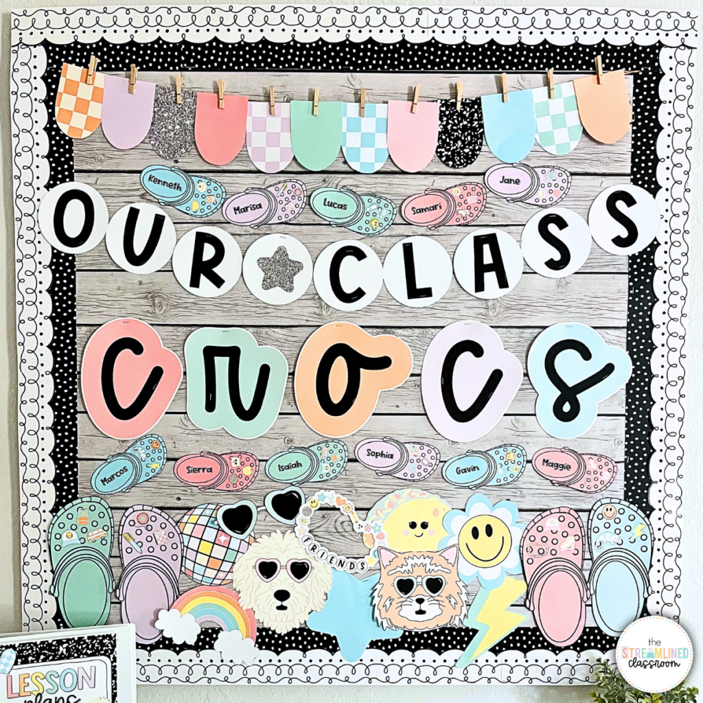 A colorful classroom bulletin board with the phrase "Our Class Crocs" in bold, playful lettering. Surrounding the text are illustrated Crocs, each labeled with a student's name. The display includes pastel and retro-themed accents, such as a rainbow, smiley faces, and a dog and cat wearing sunglasses. The border features black-and-white scalloped edges, and a mini pennant banner hangs across the top.