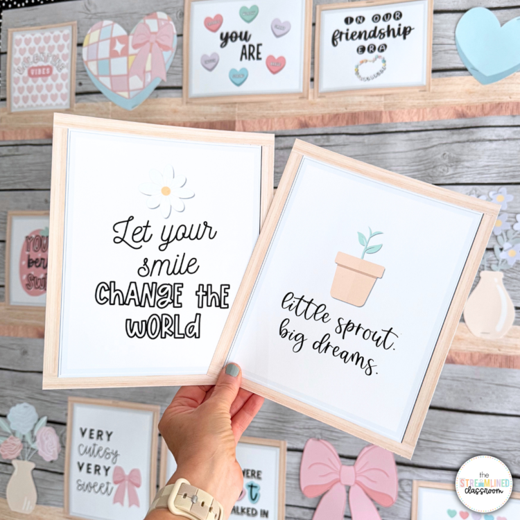 Hand holding two printable framed quotes: “Let your smile change the world” and “Little sprout, big dreams.” Boho classroom decor with framed inspirational phrases and pastel backgrounds in the display behind.