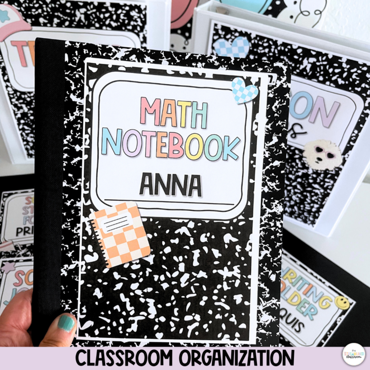 Hand holding a composition notebook with a pastel “Math Notebook” label for Anna. Background includes additional labeled binders and classroom organization materials.