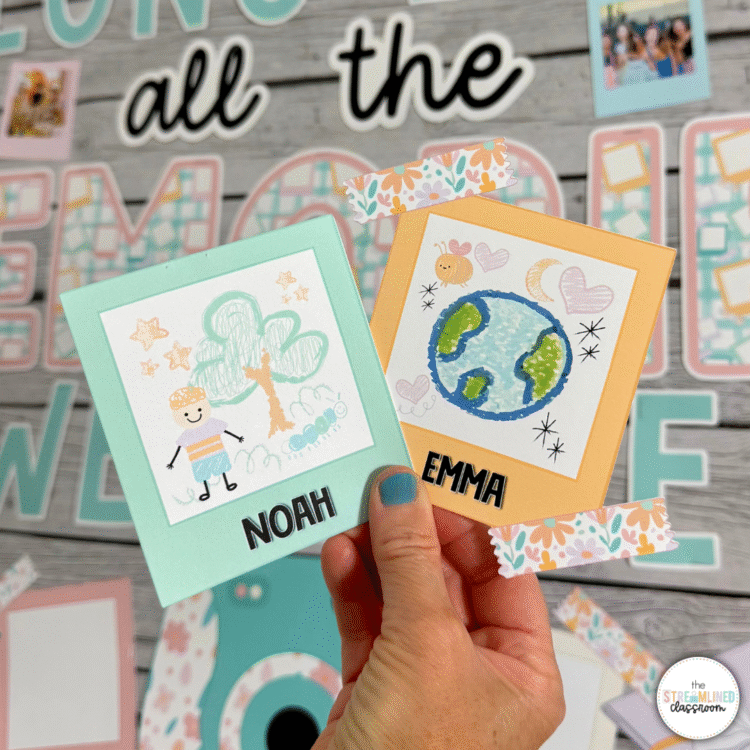 Two student-drawn Polaroid crafts labeled 'Noah' and 'Emma,' held in front of the bulletin board. The artwork includes a tree scene and a drawing of Earth with hearts and stars.